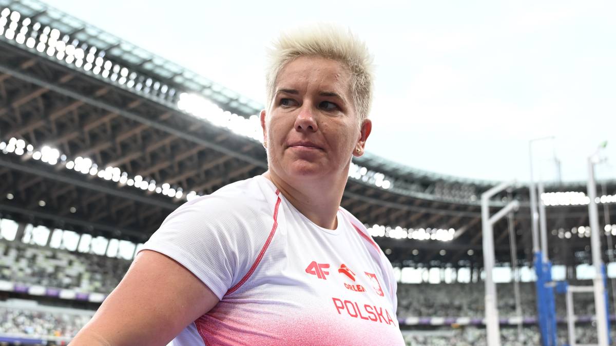 Anita Włodarczyk, polska lekkoatletka, w biało-różowej koszulce sportowej, z krótkimi blond włosami, w tle trybuny stadionu.