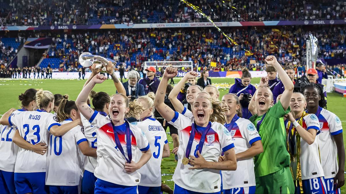 Drużyna piłki nożnej kobiet w strojach angielskich świętuje zwycięstwo, trzymając trofeum, na tle stadionu z kibicami.