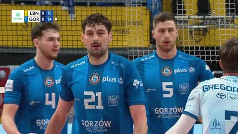 Trzej siatkarze w niebieskich koszulkach z numerami 4, 21 i 5, stojący na boisku siatkarskim podczas meczu.