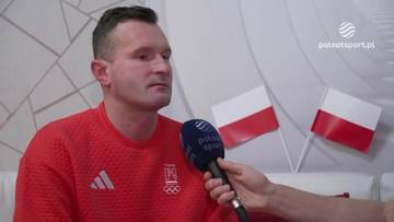 Mężczyzna w czerwonej bluzie z dwoma małymi polskimi flagami w tle.