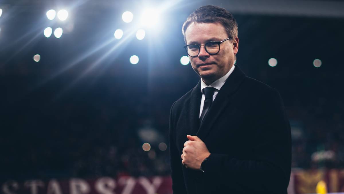 Jarosław Kr&oacute;lewski, prezes Wisły Krak&oacute;w, w eleganckim garniturze na tle stadionu.