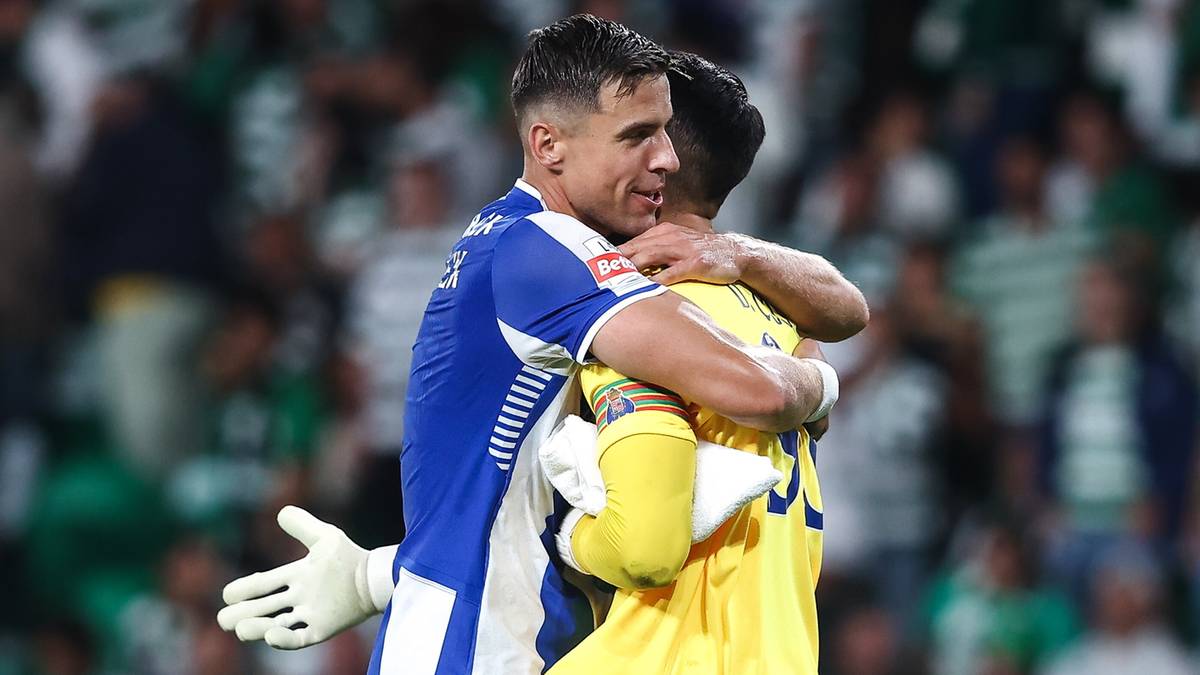 Dw&oacute;ch piłkarzy w kolorowych strojach obejmuje się na boisku piłkarskim, jeden w niebieskiej koszulce z białymi pasami, drugi w ż&oacute;łtej, obaj mają rękawice bramkarza.