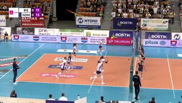 Mecz siatk&oacute;wki BKS Bostik ZGO Bielsko-Biała - Eco Harpoon LOS Nowy Dw&oacute;r. Zawodniczka w białej koszulce wykonuje atak nad siatką, podczas gdy jej koleżanka z drużyny w białej koszulce i czarnych spodenkach przygotowuje się do obrony. Na boisku widać sześć zawodniczek, dwie z nich w akcji. Na trybunach zgromadzeni są widzowie. Na telebimie widnieje wynik 0:11 dla BKS i 0:13 dla LOS.