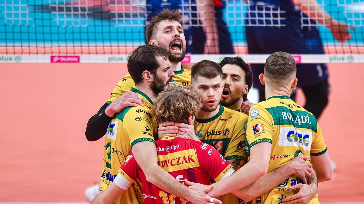 Drużyna Aluron CMC Warta Zawiercie świętująca zwycięstwo w siatkówce, gracze w żółto-zielonych strojach przytulają się.