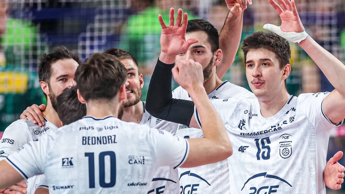 Grupa siatkarzy w białych strojach świętuje na boisku, unosząc ręce w geście radości.