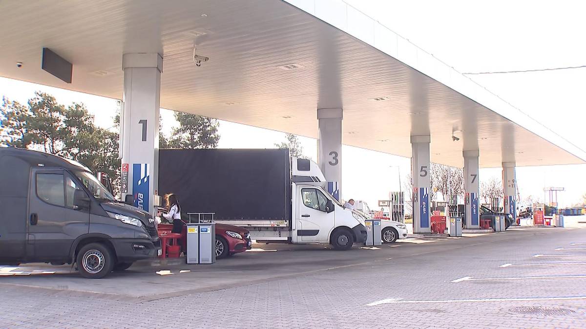 Stacja paliw z widocznymi dystrybutorami, samochodami i zadaszeniem.