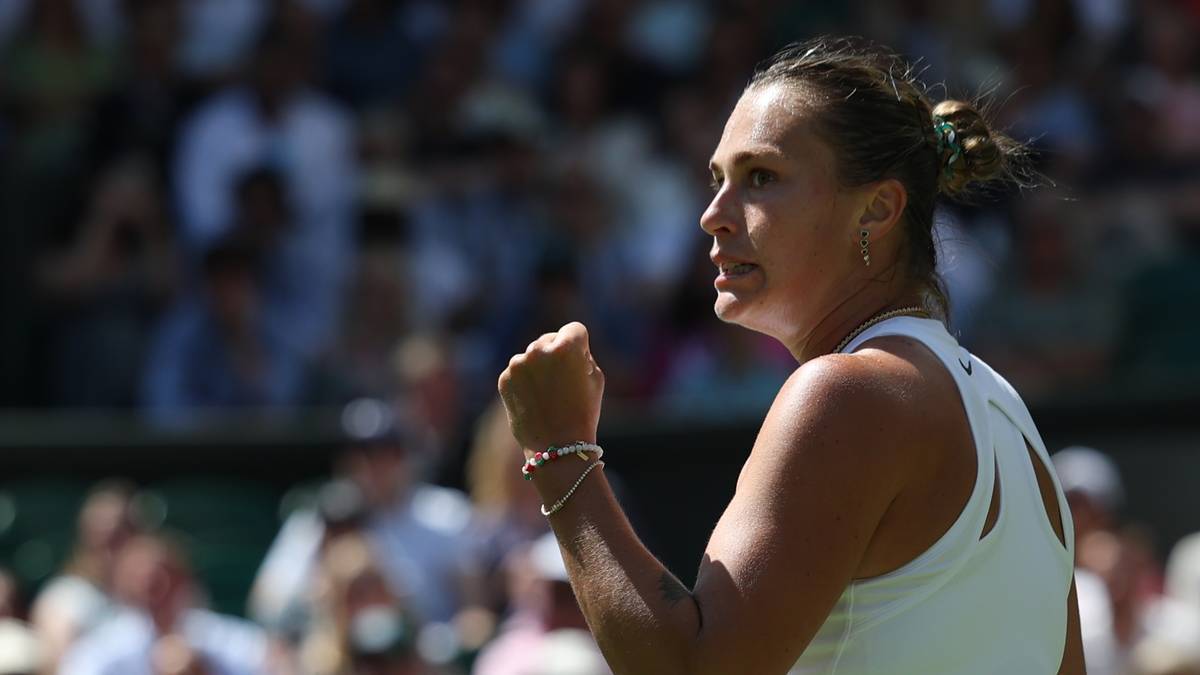 Aryna Sabalenka, zawodniczka tenisa, zaciśniętą pięścią w geście triumfu, w białym stroju sportowym.