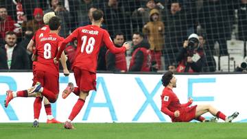 Piłkarze w czerwonych strojach świętują bramkę, jeden z nich leży na boisku.