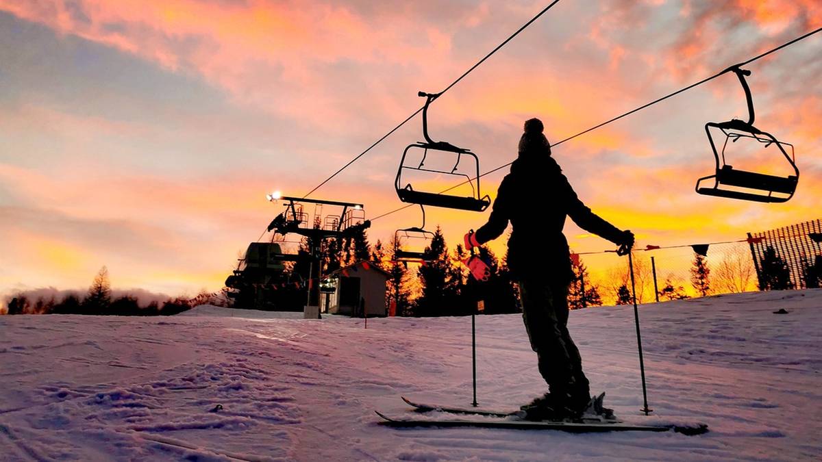 Narciarz na stoku narciarskim z wyciągiem krzesełkowym w tle podczas zachodu słońca.