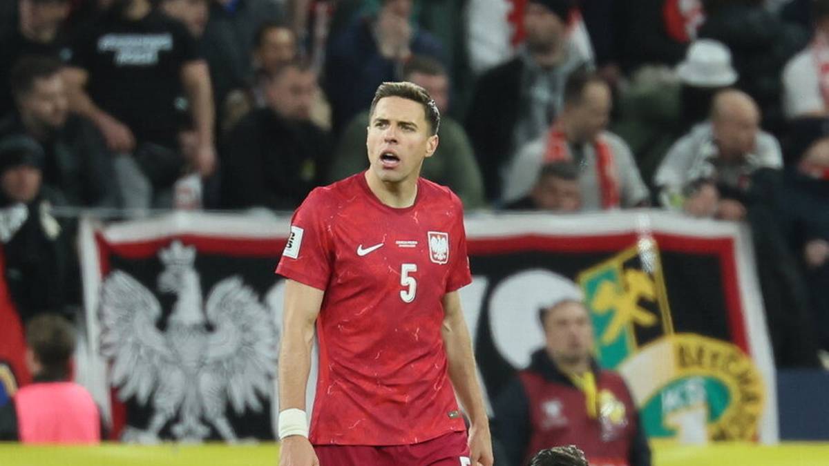 Piłkarze reprezentacji Polski w czerwonych strojach meczowych na boisku piłkarskim, z widokiem na trybuny kibic&oacute;w w tle.