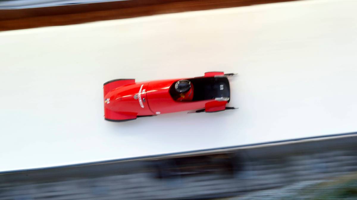 Czerwony monobob z zawodniczką w środku pędzący po torze saneczkowym.