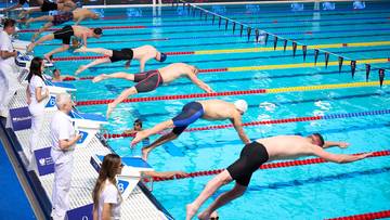 Zawodnicy pływacy startują w wyścigu z bloków startowych w basenie.