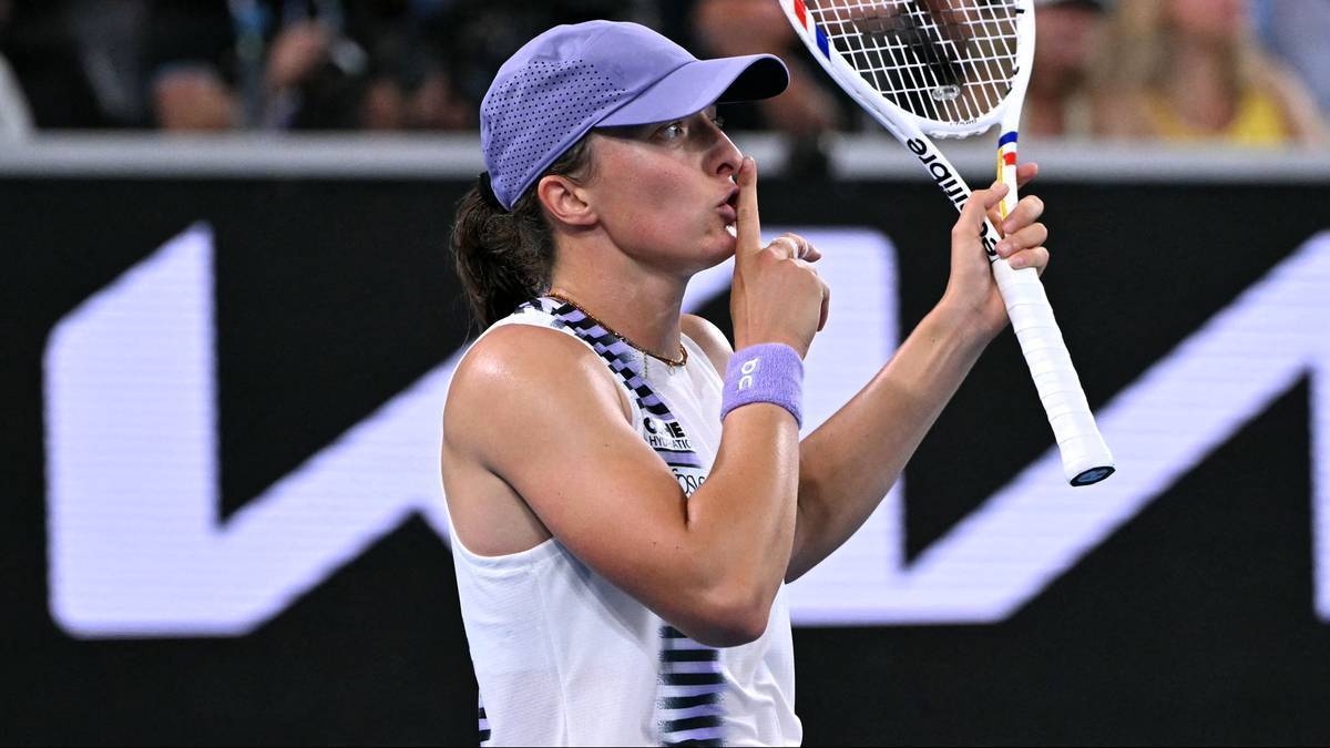 Tenisistka w białej koszulce i fioletowej czapce pokazuje gest ciszy, trzymając rakietę tenisową.