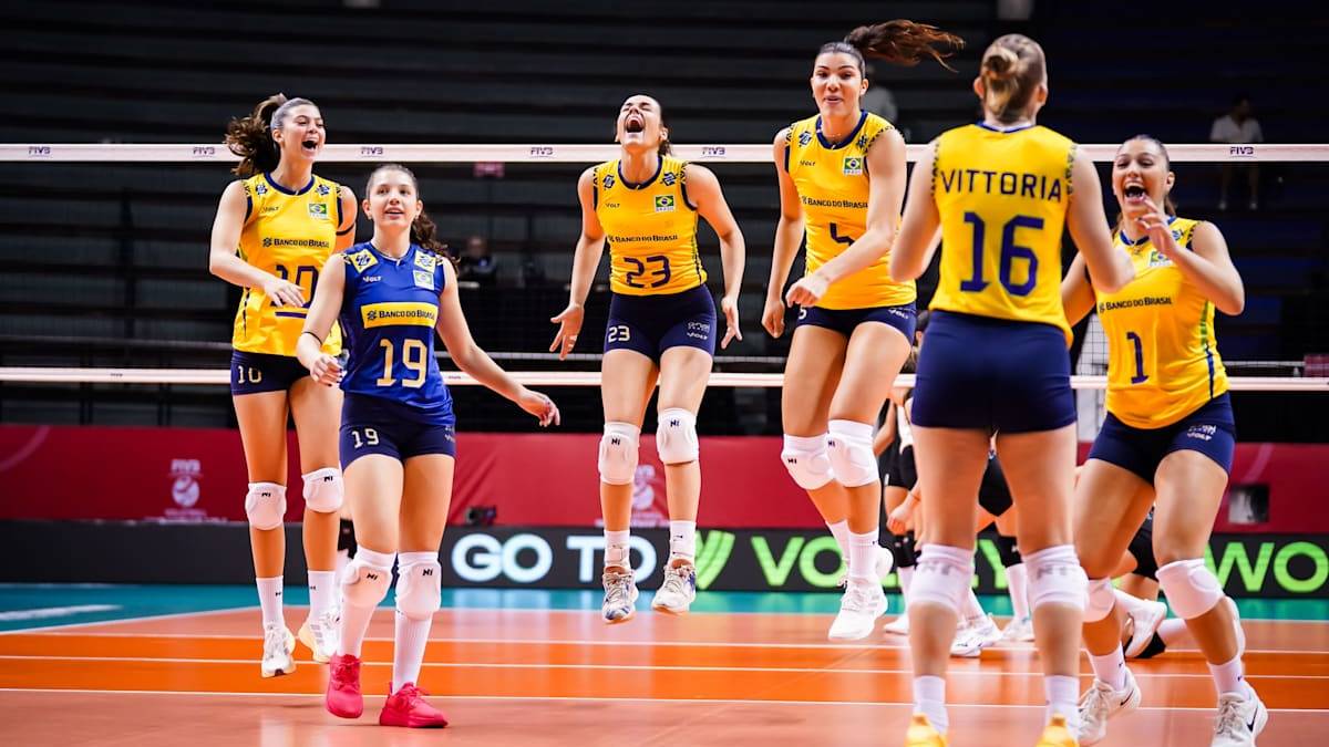 Grupa siatkarek w żółtych strojach z numerami na plecach, w tym zawodniczka z numerem 19, świętuje zwycięstwo lub punkt na boisku siatkarskim.