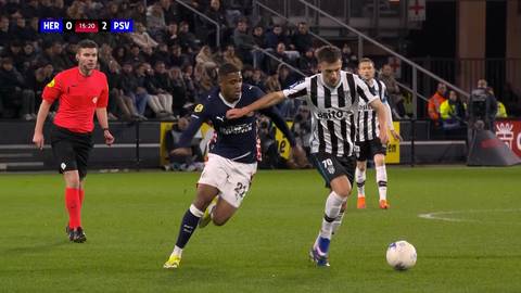 Piłkarze walczący o piłkę na boisku podczas meczu piłki nożnej. Jeden z nich nosi granatowo-białą koszulkę, drugi biało-czarne pasy. W tle widać trybuny z kibicami i sędziego.