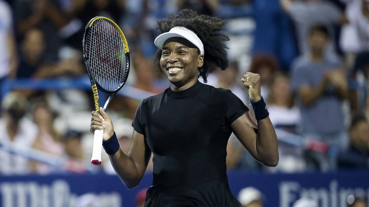 Venus Williams uśmiecha się, trzymając rakietę tenisową i zaciskając pięść. Jest ubrana w czarny strój sportowy.