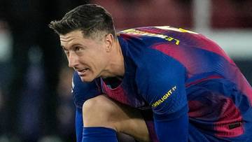 Piłkarz Robert Lewandowski na kolanach na boisku piłkarskim, wiążący sznur&oacute;wki w bucie.