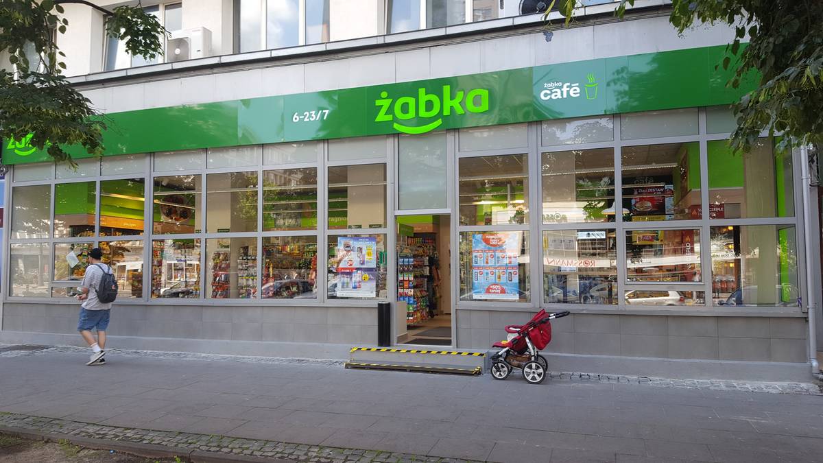 Fasada sklepu Żabka z zielonym logo i napisem "żabka cafe" na zielonym tle.