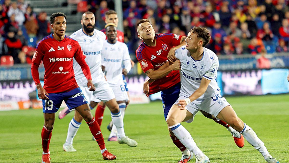 Dw&oacute;ch piłkarzy walczących o piłkę na boisku piłkarskim. Jeden w czerwonej koszulce z numerem 19, drugi w białej.