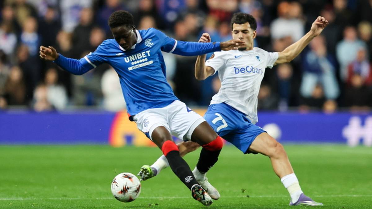 Dwóch piłkarzy walczy o piłkę na boisku. Jeden w niebieskiej koszulce z napisem 'UNIBET', drugi w białej koszulce z numerem 77.