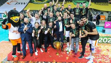 Drużyna siatkarzy Jastrzębskiego Węgla świętuje zdobycie trofeum, pozując do zdjęcia z pucharem i maskotką klubu.