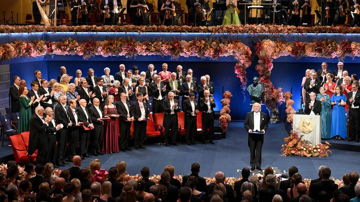 Scena z uroczystości wręczenia Nagród Nobla, na której szwedzki monarcha wręcza dyplomy laureatom w obecności publiczności.