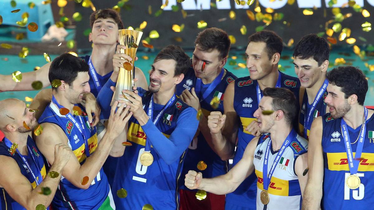 Drużyna siatkarzy w niebieskich strojach z złotymi medalami na szyjach, świętująca zwycięstwo i trzymająca puchar.