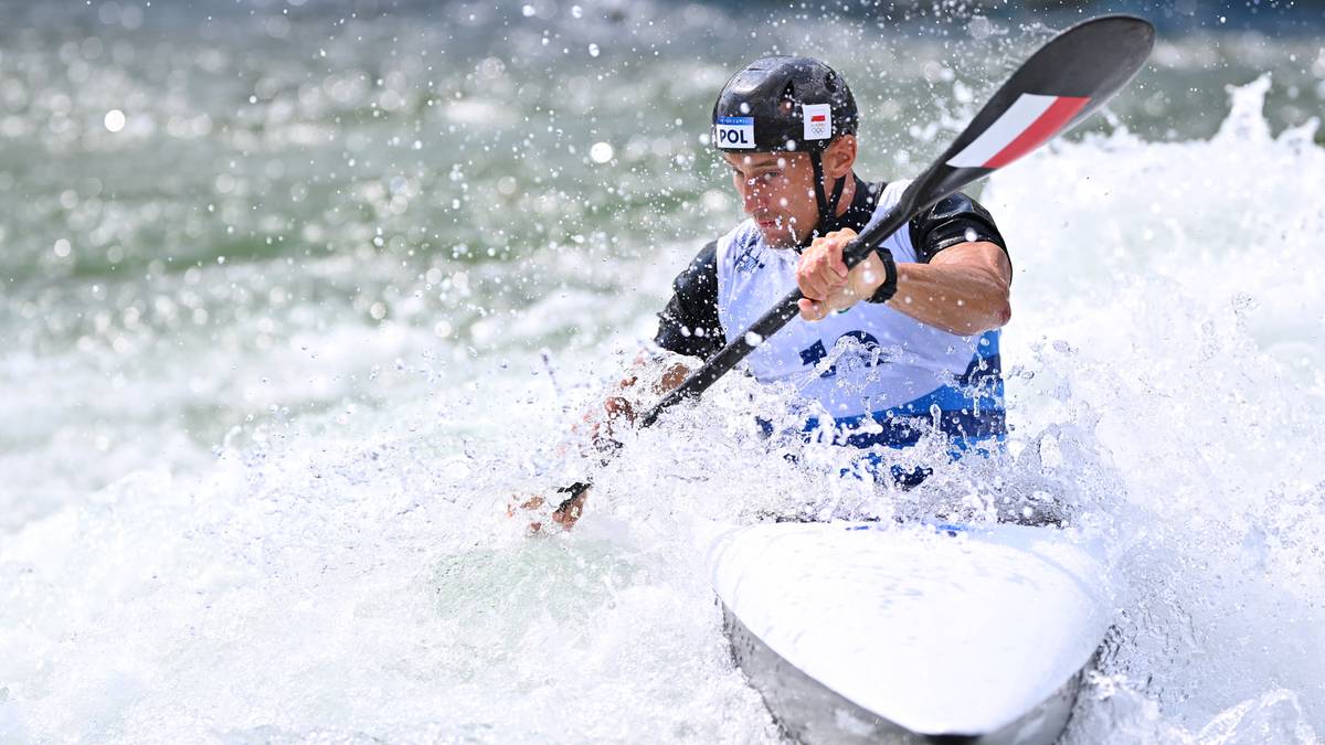 Mężczyzna w kasku i kamizelce ratunkowej wiosłuje kajakiem przez wodę.