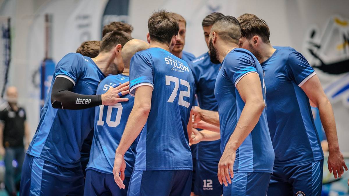Drużyna siatkarzy Cuprum Stilon Gorzów w niebieskich strojach sportowych stoi w kółku, trzymając się za ramiona.