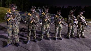 Grupa żołnierzy niemieckiej armii w pełnym umundurowaniu i z bronią na tle pojazdu wojskowego nocą.