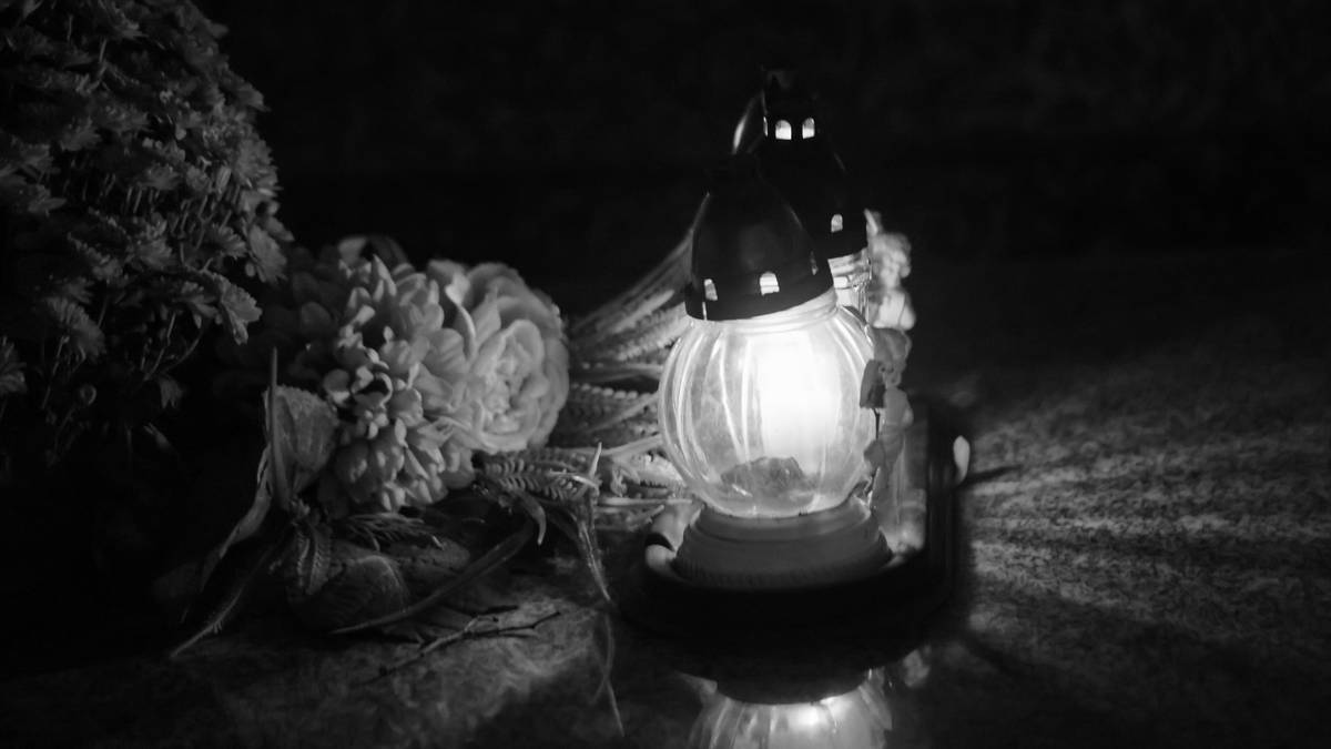 Płonąca znicz na ciemnym tle, obok wiązanka kwiatów.