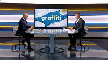 Dw&oacute;ch mężczyzn w garniturach siedzi przy okrągłym stole w studiu telewizyjnym. Na ekranie za nimi wyświetlany jest napis "graffiti".