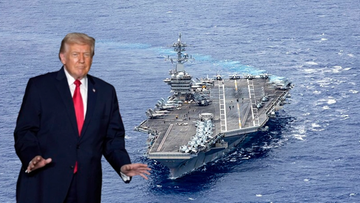 Zdjęcie przedstawia Donalda Trumpa stojącego na pierwszym planie po lewej stronie, z wyciągniętymi rękami. W tle, na wodzie, widoczny jest duży amerykański lotniskowiec.