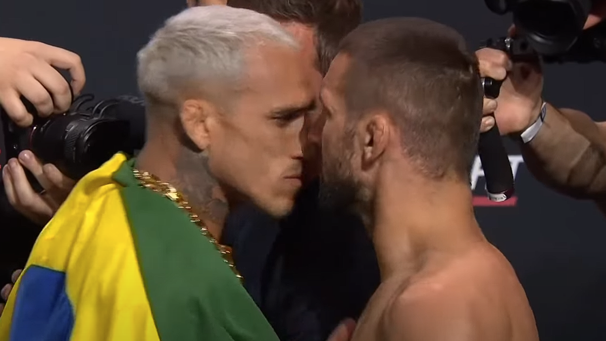 Dwóch mężczyzn, Mateusz Gamrot i Charles Oliveira, stoją naprzeciwko siebie, z twarzami bardzo blisko, podczas oficjalnego ważenia przed walką UFC. Obaj są skupieni i zdeterminowani.