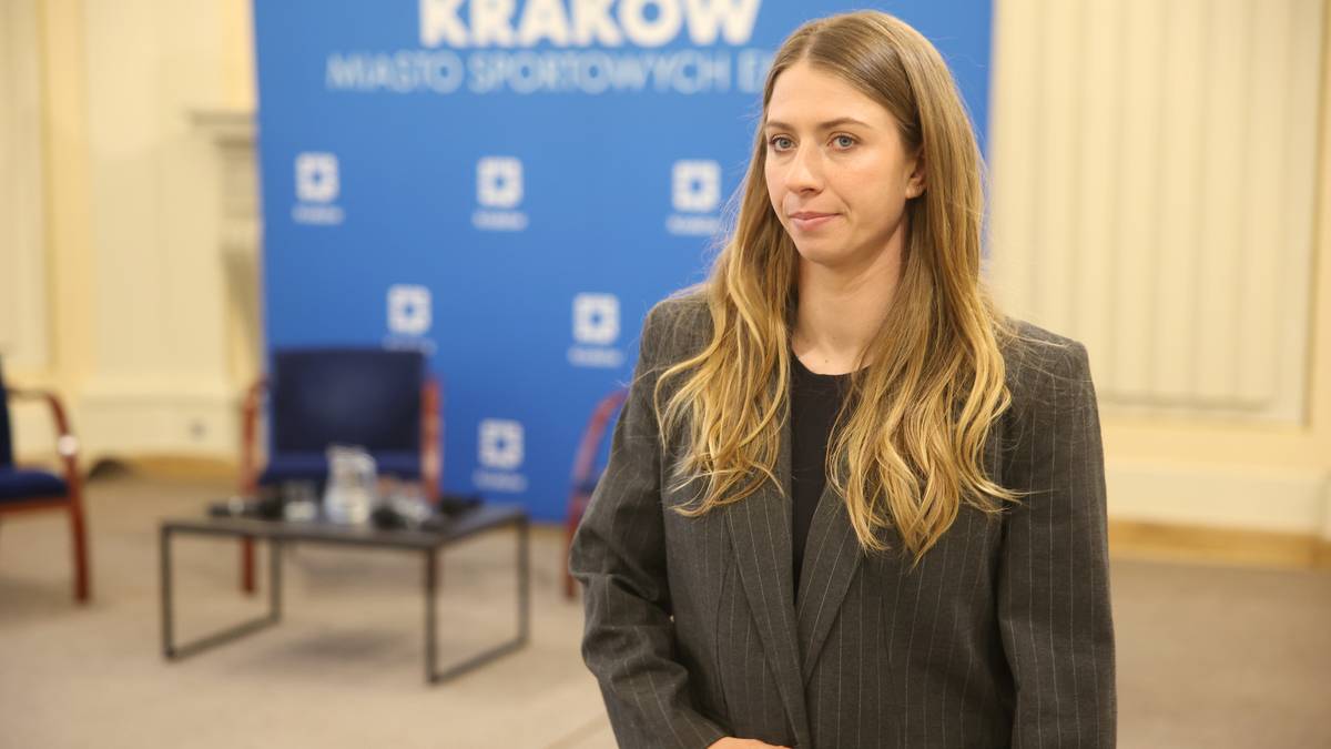 Portret Klaudii Zwolińskiej w garniturze, stojącej przed niebieskim banerem z napisem "KRAK&Oacute;W MIASTO SPORTOWYCH EMOCJI".