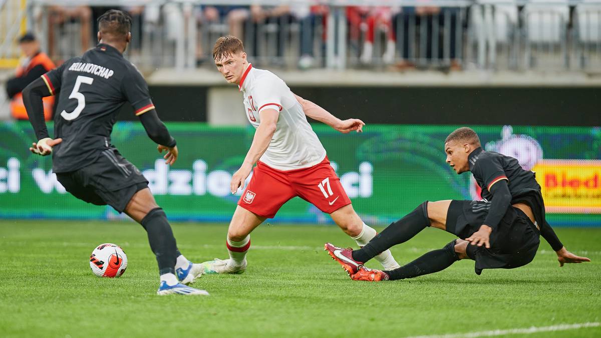 Trzech piłkarzy na boisku podczas meczu, jeden z nich biegnie z piłką, dwóch pozostałych próbuje go powstrzymać.