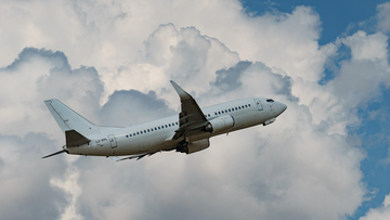 Biały samolot pasażerski Boeing 737 wznoszący się na tle błękitnego nieba z białymi chmurami.