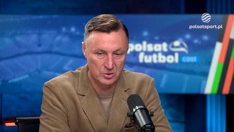 Mężczyzna w brązowej marynarce mówi do mikrofonu na tle studia telewizyjnego z logo Polsat Sport.