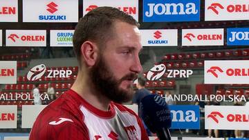 Mężczyzna z brodą w czerwonej koszulce sportowej, udzielający wywiadu.