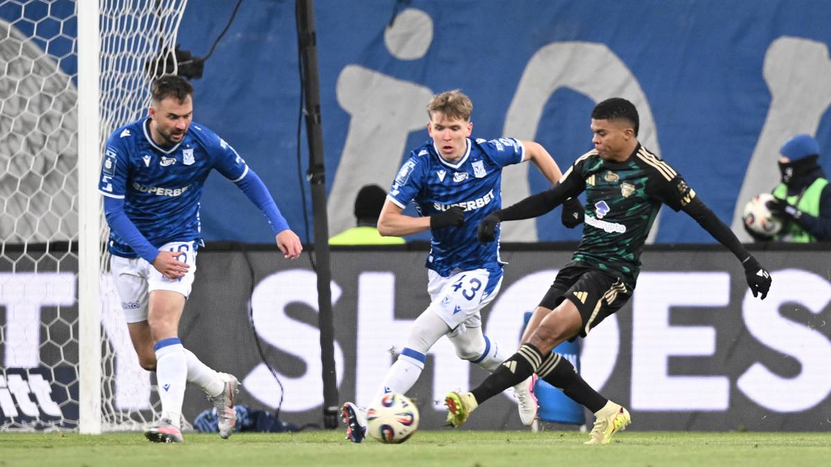 Piłkarze w niebieskich i zielonych strojach rywalizują o piłkę na boisku.