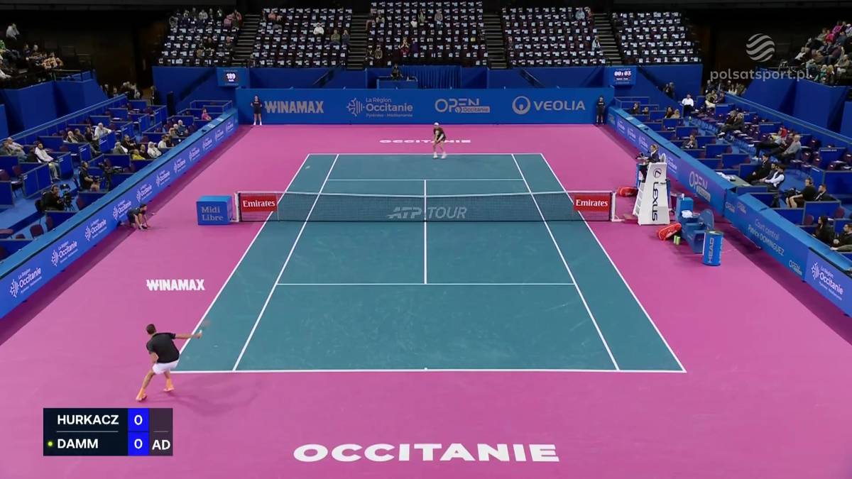 Mecz tenisa ziemnego Huberta Hurkacza z Martinem Damem Jr. na korcie z r&oacute;żową nawierzchnią i niebieskimi bandami. Widownia zasiada na niebieskich trybunach.
