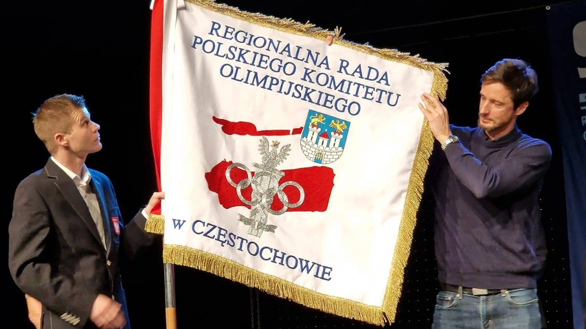 Dwóch mężczyzn prezentuje sztandar Regionalnej Rady Polskiego Komitetu Olimpijskiego w Częstochowie.