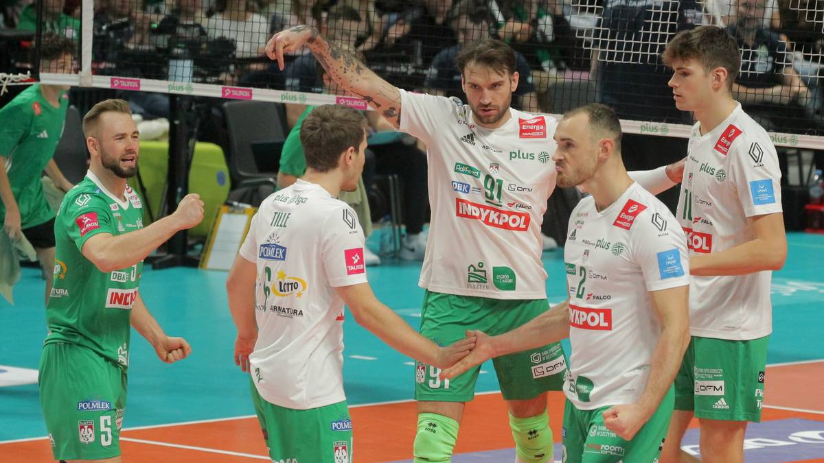 Siatkarze w zielonych i białych strojach rozmawiają na boisku.