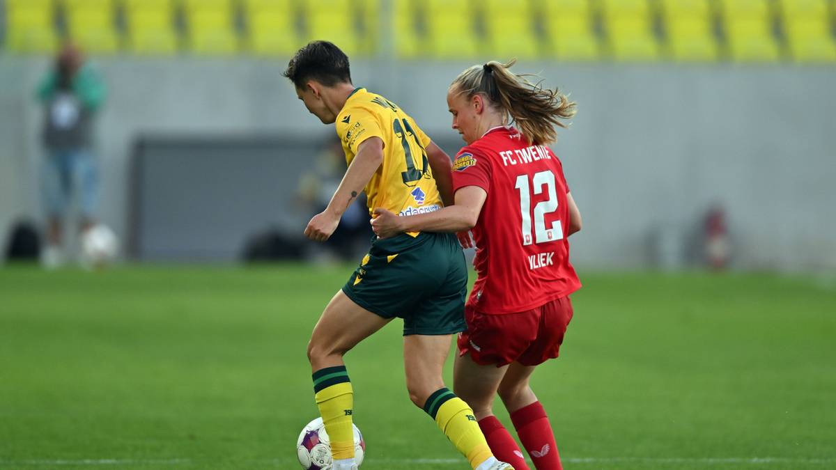 Dwóch piłkarzy w akcji na boisku, jeden w żółtej koszulce, drugi w czerwonej.