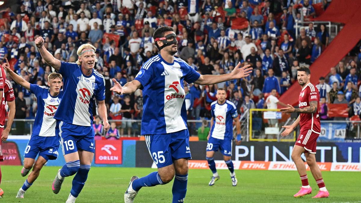 Piłkarz w niebiesko-białej koszulce z numerem 35 na plecach cieszy się po zdobyciu bramki, na drugim planie widoczni inni zawodnicy i kibice na trybunach.