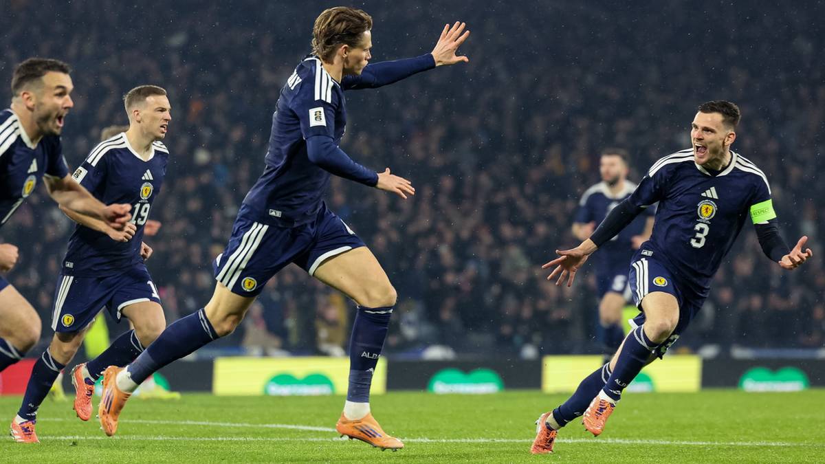 Piłkarze reprezentacji Szkocji w granatowych strojach cieszą się z bramki, jeden z zawodników biegnie z uniesionymi rękami, inni podbiegają do niego.