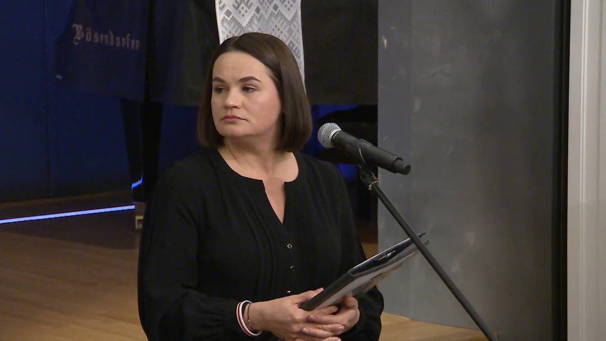 Kobieta w czarnej bluzce z dokumentami w rękach przy mikrofonie.