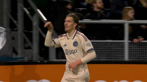 Piłkarz Ajax Amsterdam w białej koszulce z ż&oacute;łtymi akcentami i logo Ziggo, unosi prawą rękę w geście radości.