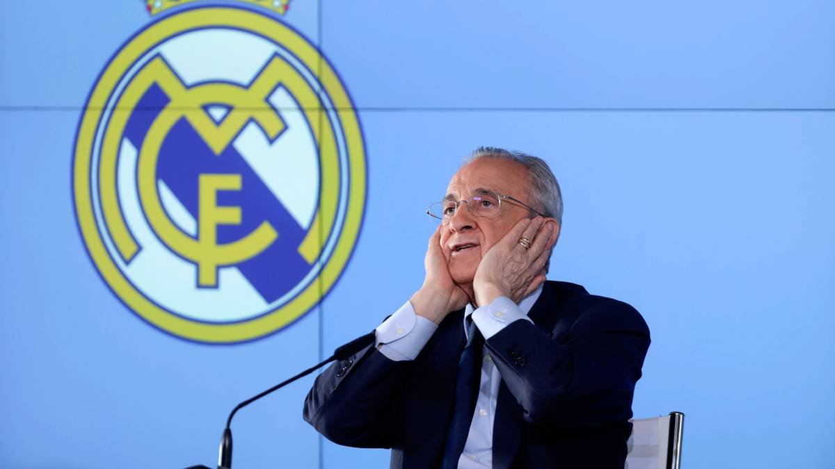 Florentino Perez, prezes Realu Madryt, z rękami przy uszach na tle herbu klubu.