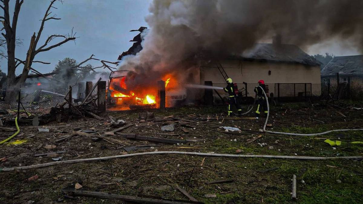 Grupy strażaków walczące z płonącymi ruinami budynków i pojazdu, z których unosi się kłąb dymu.